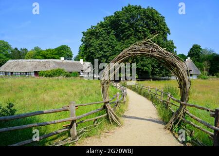 Lyngby, Dänemark - Juli 2021: Hölzerner Torbogen am Eingang des alten Dänemarks, Freilichtmuseum (Frilandsmuseet) mit alten Gebäuden im Hintergrund. Stockfoto