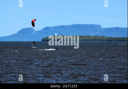 In der Bucht von Mission Marsh sind zwei Männer im Lake Superior beim Windsurfen und Parasailing, im Hintergrund der Sleeping Giant und eine Welcome Island. Stockfoto