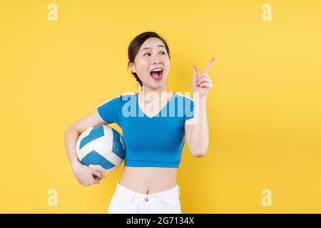 Portrait von jungen dynamischen Mädchen hält Ball in der Hand isoliert auf gelbem Hintergrund Stockfoto