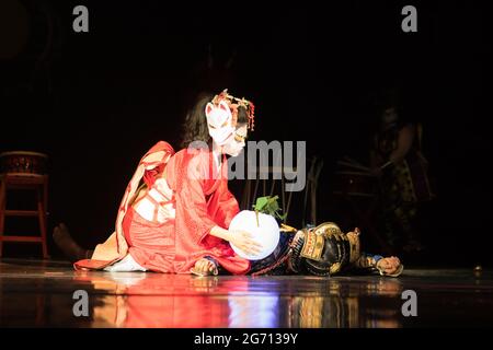 Die Japanerin trauert um einen toten Samurai, der auf ihren Knien sitzt, wobei er im Dunkeln eine Lampe am Körper hat. Traditionelle japanische Darbietung. Stockfoto