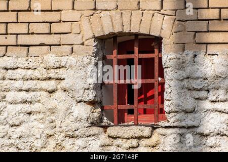Blick auf eine Backsteinmauer mit einem kleinen alten Balkenfenster Stockfoto
