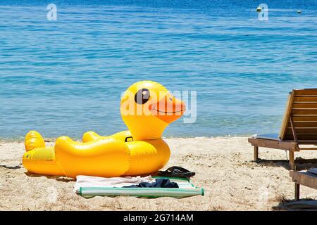 Gelbe, aufblasbare Ente, die am Strand vor dem Meer sitzt. Stockfoto