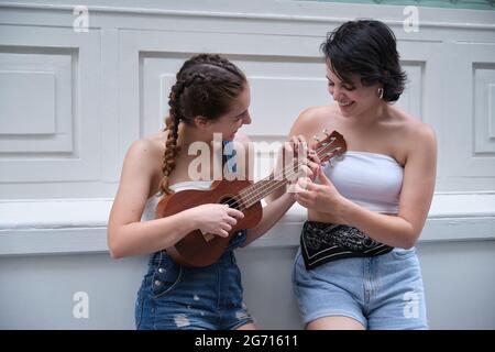 Eine Frau, die anderen beibringt, wie man Ukelele auf einer Stadtstraße spielt. Musik im Freien. Stockfoto