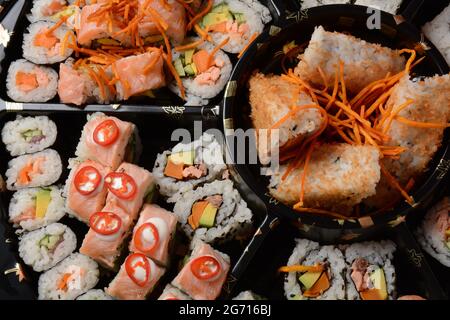 Set von Sushi-Rollen auf einer schwarzen Kunststoffplatte, verziert mit Sojasauce und Gewürzen. Bereit zur Lieferung Stockfoto