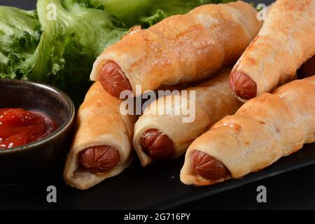 Wurstbrötchen. Weich gebackenes Brötchen (Teig) gefüllt mit Schweinewurst für Fast-Food-Frühstück oder Kaffeepause. Wurstrolle (Hot Dog). Stockfoto