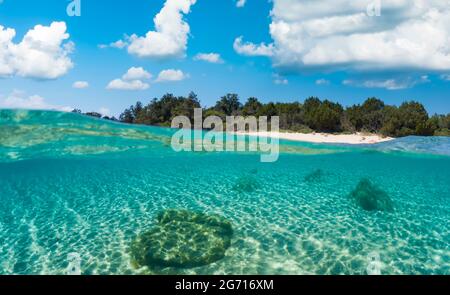 Split-Shot, Over-under-Shot. Halb unter Wasser halb Himmel mit einem türkisfarbenen Wasser und einem weißen Sandstrand in der Ferne an einem sonnigen Tag. Stockfoto