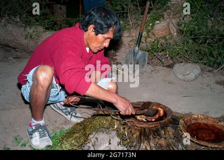 Nazca, Peru - 19 2010. Juli: Traditionelles Pachamanca-Abendessen, das von einem indigenen Mann in der Nacht zubereitet wird, indem er im Boden kocht. Stockfoto