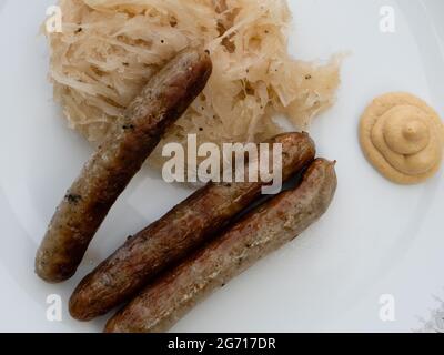 Nürnberger Grillwurst oder Nürnberger Rostbratwurst mit Sauerkraut oder saurem Kohl und Senf auf einem weißen Teller aus nächster Nähe Stockfoto