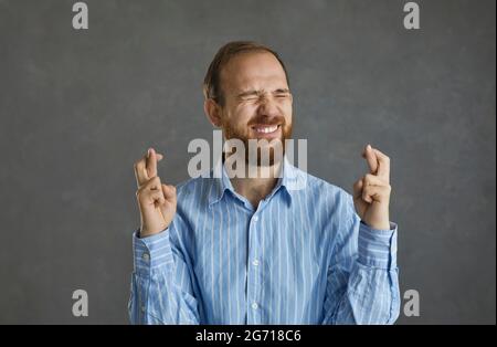 Junger Mann, der die Daumen drückt, an Glück glaubt und auf das Beste hofft Stockfoto