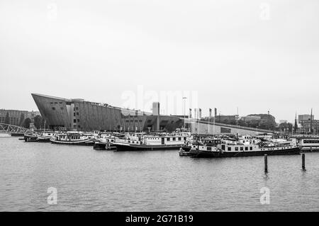 AMSTERDAM, NIEDERLANDE. 06. JUNI 2021. Schöner Blick auf einen Schiffskanal und Brücken. Schwarzweiß-Fotografie. Kleine Boote, Schiffe und Bargen Stockfoto