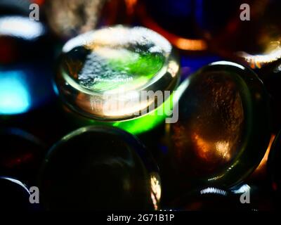 Nahaufnahme eines flachen runden Edelsteins, auf dem Licht reflektiert wird, umgeben von anderen bunten Edelsteinen Stockfoto