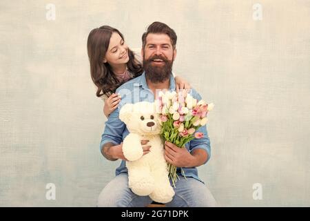 Freut Euch, Euch zu feiern. Alles gute zur Familie feiern Geburtstag. Kleines Mädchen gratuliert bärtigen Mann. Kleine Tochter und Vater halten Blumen und Spielzeug Stockfoto