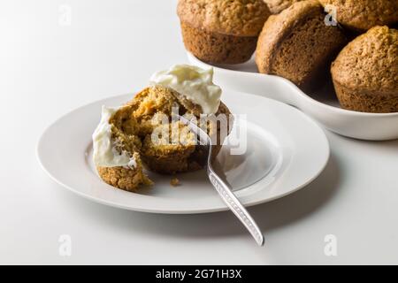 Muffin mit Karotten-Zimt-Kuchen und Joghurt auf weißem Servierteller mit Muffins im Hintergrund isoliert auf weiß mit Platz zum Kopieren - Nahaufnahme Stockfoto