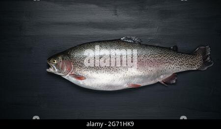 Frischer roher Lachs, roter Fisch auf einem schwarzen Holztisch. Kreatives Layout aus Fisch, Meeresfrüchten, Draufsicht, Flachlagerung Stockfoto