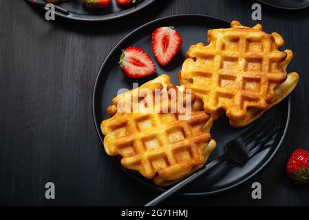 Waffeln mit Erdbeeren auf einem schwarzen Holztisch. Stockfoto