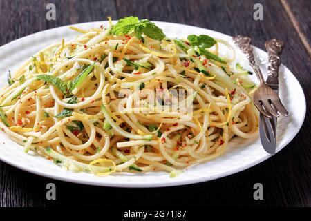 Sommer-Spaghetti alla carrettiera mit Minzblättern, Zitronenschale, Pecorino-Käse, Chilischoten-Flocken, Petersilie und geriebenen Zucchini auf einem weißen Teller Stockfoto