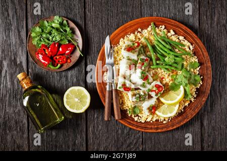 Bacalhau com todos, Kabeljau mit Bulgur, gedämpfte grüne Bohnen, bestreut mit scharfer Chilischote und Frühlingszwiebeln auf einem rustikalen Teller, auf einem Holztisch, por Stockfoto