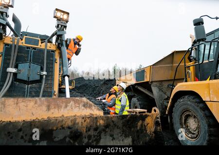 Schwere Maschinen und Arbeiter in Grube des Steinbruchs schreien einander an, weil der Lärm unerträglich ist Stockfoto