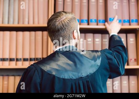 Ein junger Anwalt mit Robe, der bereit ist, vor Gericht zu gehen, ergreift einige Bücher aus der Bibliothek Stockfoto