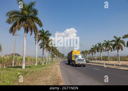 Verkehr auf dem guatemaltekischen Tiefland mit Palmen und Vulkan in der Ferne Stockfoto