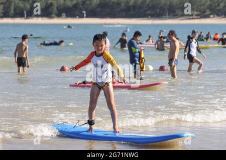 Sanya, Chinas Provinz Hainan. Juli 2021. Touristen surfen im Wasser des Fischerdorfes Tenghai in Sanya, südchinesische Provinz Hainan, 8. Juli 2021. Das in der Haitang Bucht von Sanya gelegene Fischerdorf Tenghai hat seit 2018 viele Touristen durch die Entwicklung von Tourismus-, Surf- und Gastfamilien-Industrien angezogen. Quelle: Zhang Liyun/Xinhua/Alamy Live News Stockfoto