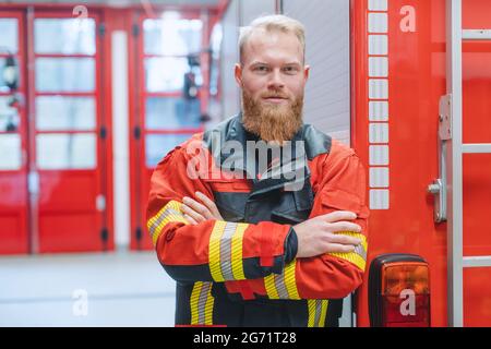 Entschlossener junger Feuerwehrmann vor einem Feuerwehrauto In der Aufseherin Stockfoto