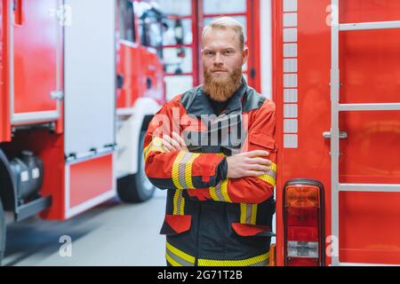 Entschlossener junger Feuerwehrmann vor einem Feuerwehrauto In der Aufseherin Stockfoto