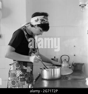 Junge hübsche Frau trägt Schürze Kochen Mahlzeit auf einem alten Stil Gaskocher 60er Jahre ungarn Stockfoto