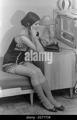 Junge Frau in Mini-Camisole, die einen Anruf über Festnetz neben analogem Radio 1960er ungarn Stockfoto