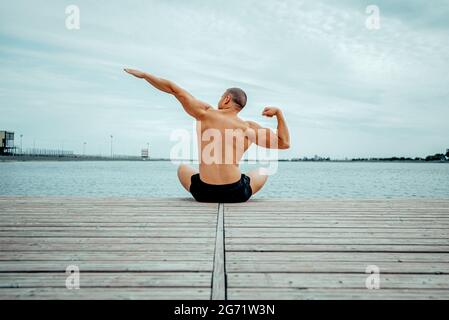 Starker, muskulöser Erwachsener macht Yoga auf dem See. Das Konzept eines gesunden Lebensstils. Stockfoto