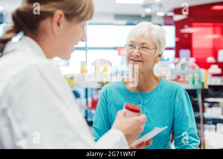 Ältere Frau in der Apotheke das Gespräch mit dem Chemiker oder Apotheker erklären Wirkungen einer Droge Stockfoto