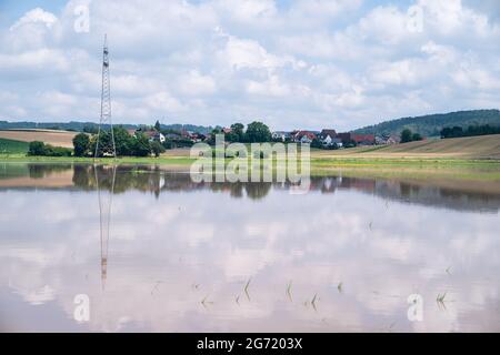 Gleusdorf, Deutschland. Juli 2021. Die Landschaft spiegelt sich in der Wasseroberfläche eines überfluteten Feldes wider. Teile von Franken sind aufgrund des hohen Wassers von gestern noch unter Wasser. Quelle: Nicolas Armer/dpa/Alamy Live News Stockfoto