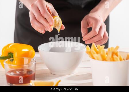 Hände drücken eine Zitronenscheibe in eine Schüssel mit Zutaten Stockfoto