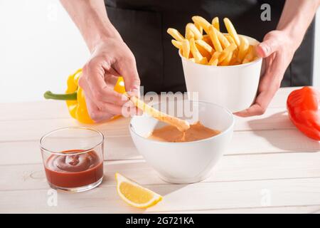 Mann hält einen Rücken mit Pommes Frites und taucht in andalouse-Sauce Stockfoto