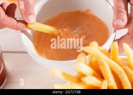 Mann taucht Pommes in hausgemachte andalouse-Sauce Stockfoto