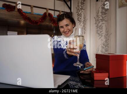Glückliche asiatische Frau trägt blauen Pullover mit einem Glas Champagner, im Gespräch mit der Familie, soziale Distanz Freund von Videokonferenz Gespräch Gespräch ein Stockfoto