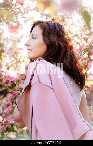 Lächelnde Frau in einer rosa Jacke auf einem Hintergrund von Kirschblüten im Garten Stockfoto