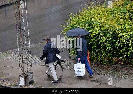 Kastrup/Dänemark. 10. Juli 2021,Seniorenpaar gehen im Regen mit Haustieren und Einkaufstaschen in Kastrup Dänemark. (Foto..Francis Joseph Dean/Dean P Stockfoto