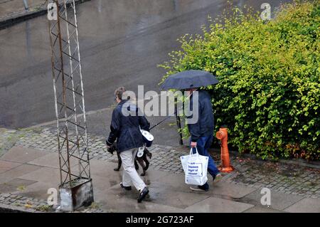 Kastrup/Dänemark. 10. Juli 2021,Seniorenpaar gehen im Regen mit Haustieren und Einkaufstaschen in Kastrup Dänemark. (Foto..Francis Joseph Dean/Dean P Stockfoto