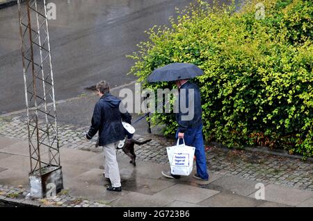 Kastrup/Dänemark. 10. Juli 2021,Seniorenpaar gehen im Regen mit Haustieren und Einkaufstaschen in Kastrup Dänemark. (Foto..Francis Joseph Dean/Dean P Stockfoto