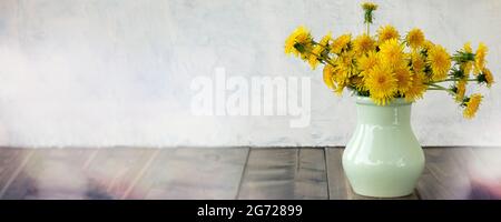 Banner mit hellen, schönen, gelben Dandelionen in Vase auf Holztisch. Gelbe Blumen im Frühling oder Sommer auf grauem strukturiertem Hintergrund. Hintergrund mit Kopierfläche. Ultimate Grey. Leuchtet. Stockfoto