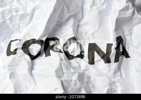 Faltiges weißes Papier mit dem Wort Corona, das aus verzerrten, schwarz gedruckten Buchstaben besteht. Ende des Coronavirus-Restriktionen-Konzepts. Stockfoto