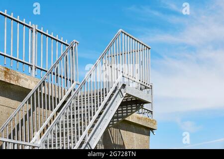 Galvanisierte Stahltreppe auf einer Betonkonstruktion gegen einen blauen Himmel mit Wolken. Bild mit Kopierbereich. Stockfoto