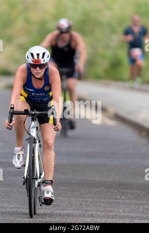 Shoeburyness, Essex, Großbritannien. Juli 2021. Aufgrund der COVID-19-Pandemie wurde der Triathlon 2020 verschoben, um wieder zurückzukehren, da die Beschränkungen für 2021 aufgehoben werden. Die Wettkämpfer, die im Shoeburyness-Gebiet östlich von Southend on Sea stattfinden, begannen den Wettbewerb mit einem 750-Meter-Schwimmen in der Themse-Mündung, bevor sie mit ihren Fahrrädern eine 20km-Fahrt durch Landstraßen und einen 5km-Lauf im Gunners Park an der Küste zurücknahmen Seine imposanten Verteidigungsstrukturen im Krieg. Das ehemalige Mod-Gebiet ist heute ein Naturschutzgebiet und beliebtes Wandergebiet. Radfahrer auf dem Straßenabschnitt Stockfoto