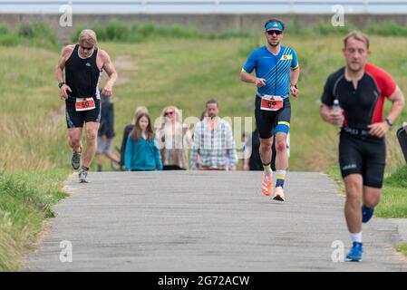 Shoeburyness, Essex, Großbritannien. Juli 2021. Aufgrund der COVID-19-Pandemie wurde der Triathlon 2020 verschoben, um wieder zurückzukehren, da die Beschränkungen für 2021 aufgehoben werden. Die Wettkämpfer, die im Shoeburyness-Gebiet östlich von Southend on Sea stattfinden, begannen den Wettbewerb mit einem 750-Meter-Schwimmen in der Themse-Mündung, bevor sie mit ihren Fahrrädern eine 20km-Fahrt durch Landstraßen und einen 5km-Lauf im Gunners Park an der Küste zurücknahmen Seine imposanten Verteidigungsstrukturen im Krieg. Das ehemalige Mod-Gebiet ist heute ein Naturschutzgebiet und beliebtes Wandergebiet Stockfoto