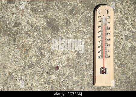 Thermometer auf Beton-Hintergrund zeigt hohe Sommertemperatur Stockfoto