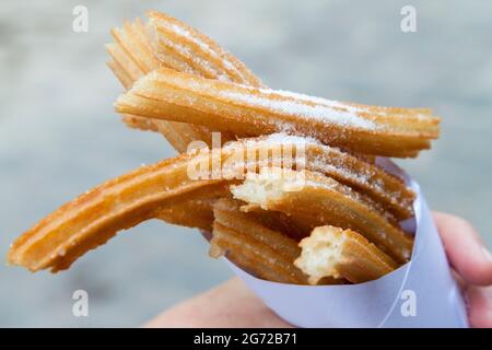 Frisch gekochte Churros, mit Zucker bestreut und in einem weißen Papierkegel hochgestapelt Stockfoto