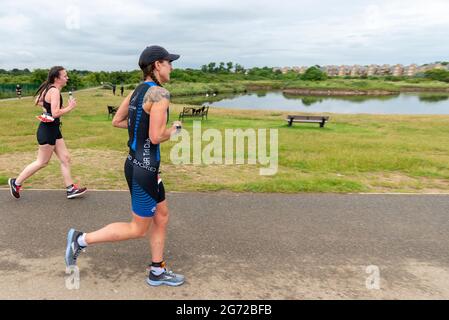 Shoeburyness, Essex, Großbritannien. Juli 2021. Aufgrund der COVID-19-Pandemie wurde der Triathlon 2020 verschoben, um wieder zurückzukehren, da die Beschränkungen für 2021 aufgehoben werden. Die Wettkämpfer, die im Shoeburyness-Gebiet östlich von Southend on Sea stattfinden, begannen den Wettbewerb mit einem 750-Meter-Schwimmen in der Themse-Mündung, bevor sie mit ihren Fahrrädern eine 20km-Fahrt durch Landstraßen und einen 5km-Lauf im Gunners Park an der Küste zurücknahmen Seine imposanten Verteidigungsstrukturen im Krieg. Das ehemalige Mod-Gebiet ist heute ein Naturschutzgebiet und beliebtes Wandergebiet Stockfoto