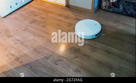 Roboter-Staubsauger und -Wischmopp reinigen die Holzoberfläche in Nahaufnahme eines Raumbodens. Modernes, intelligentes Gerät für den täglichen Haushalt. Stockfoto
