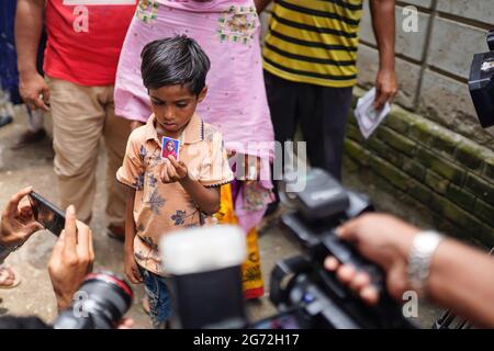 Dhaka, Bangladesch. Juli 2021. Ein Kind zeigt ein Bild seiner Mutter, die nach dem Feuer, das am Donnerstagabend in der Fabrik von Hashem Foods Ltd vor der Leichenhalle des Dhaka Medical College ausbrach, vermisst wurde. Mindestens 52 Menschen wurden tot aufgefunden, 25 weitere Verletzte und viele werden nach einem massiven Brand in einer Fabrik in die Falle getappt, die Ursache des Feuers, der im Erdgeschoss eines mehrstöckigen Gebäudes der Fabrik ausging, ist noch nicht bekannt. Kredit: SOPA Images Limited/Alamy Live Nachrichten Stockfoto